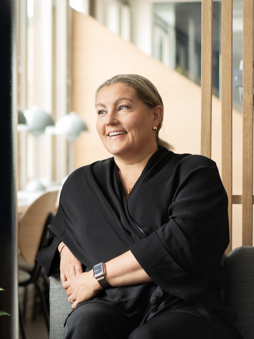 Business-tyylisesti pukeutunut nainen istuu modernissa toimistossa.